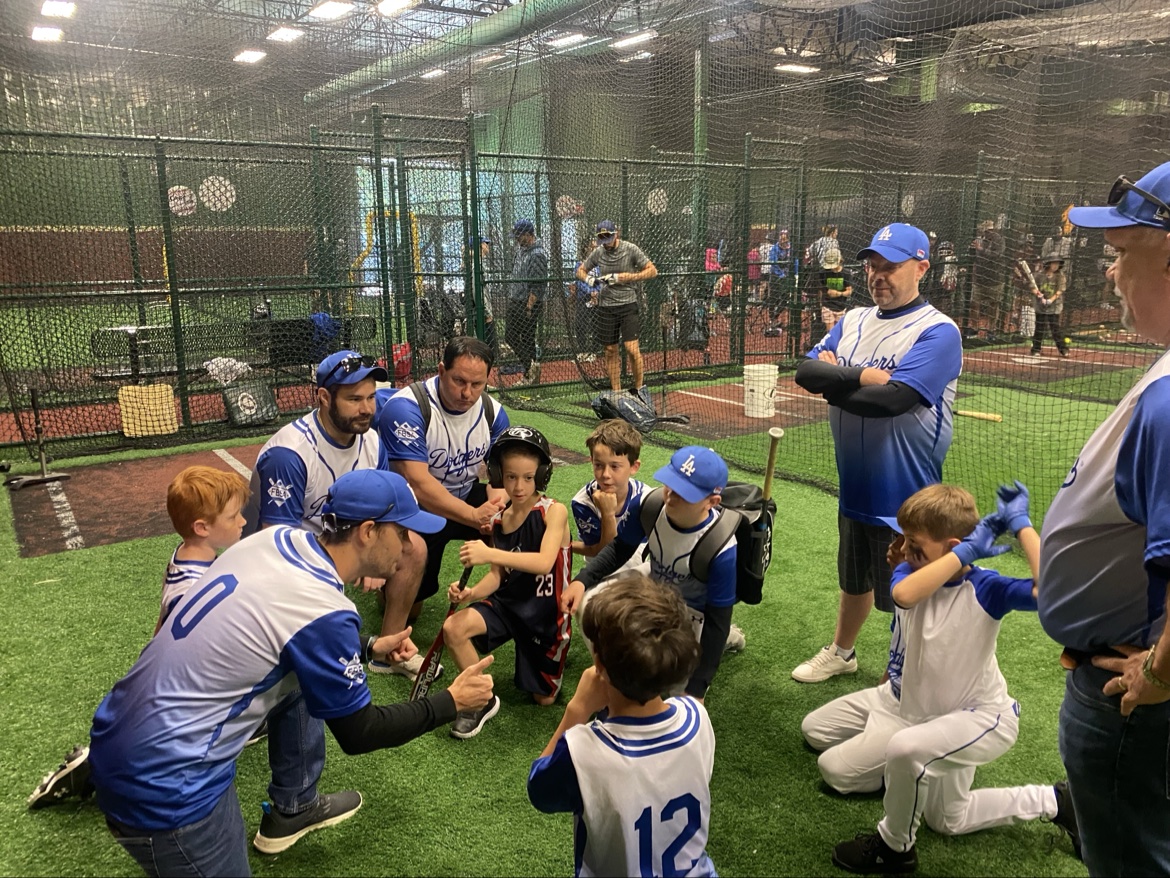 Matt Young and fellow coaches talking with young players inside an indoor batting cage