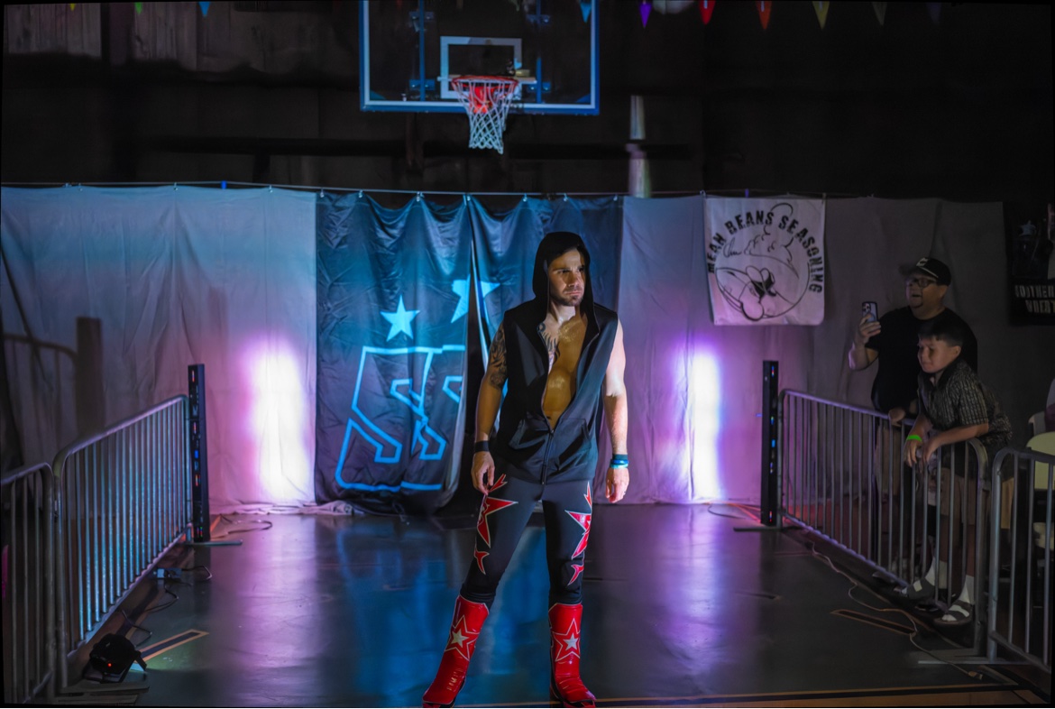 Matt Young making his entrance at his retirement match — hood up, red star boots, arena lights behind him